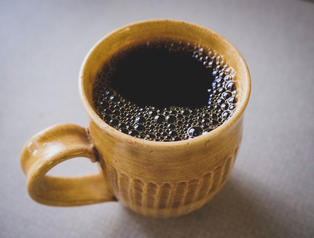 A warm cup of black coffee in a rustic ceramic mug with visible bubbles.
